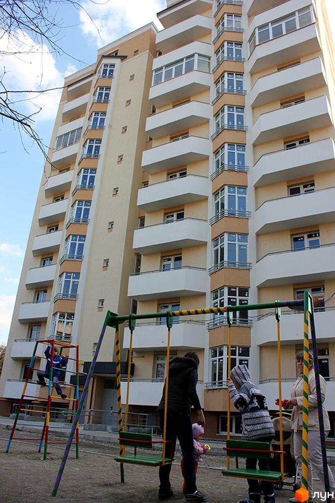 Зовнішній вигляд житлового будинку на вул. Угорська, 7а. На передньому плані дитячий майданчик з гойдалками.