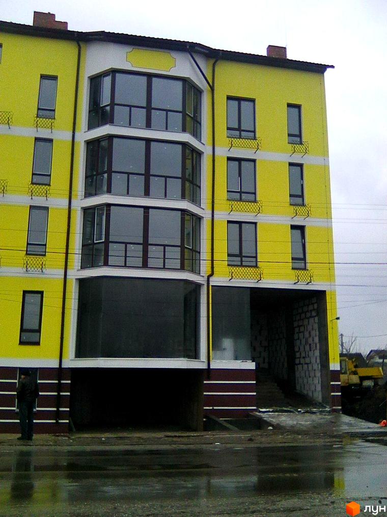 Зовнішній вигляд жовто-білої новобудови ЖК Шевченківський маєток з великими вікнами. Поруч видно будівельну техніку та облаштовану територію.