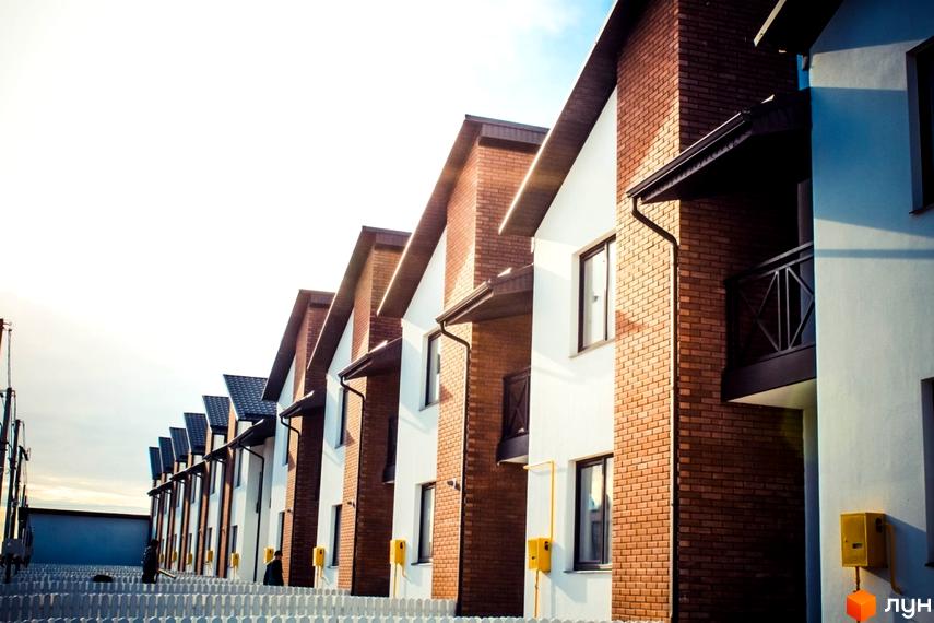 Котеджне містечко КМ Струмочок: фасади будинків з цегли та білої штукатурки, вікна, балкони та прибудинкова територія з парканом.