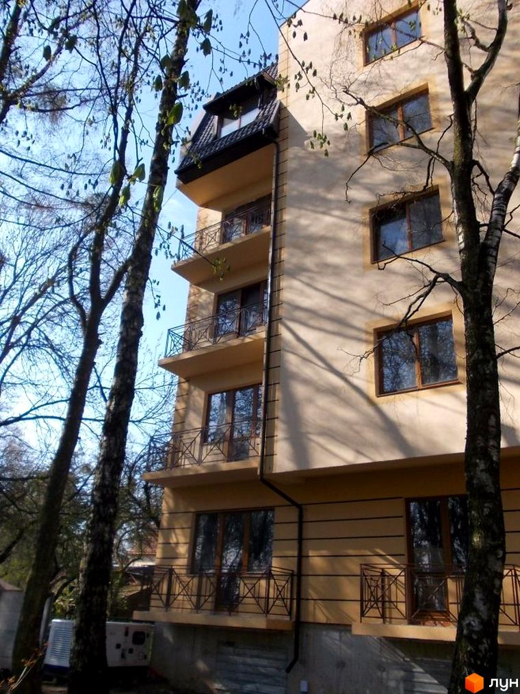 Зображення фасаду будинку на вул. Академіка Рудницького, 11б. Багатоповерхова будівля з балконами та вікнами, оточена деревами.