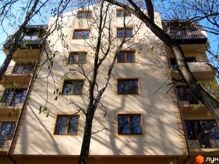 Зовнішній вигляд будинку по вул. Академіка Рудницького, 11б. Багатоповерхова будівля з вікнами, оточена деревами.