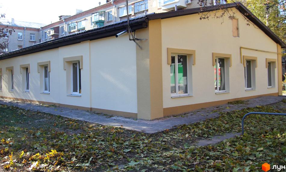 Зовнішній вигляд одноповерхового будинку з білими вікнами та бежевим оздобленням. Прибудинкова територія вкрита опалим листям.