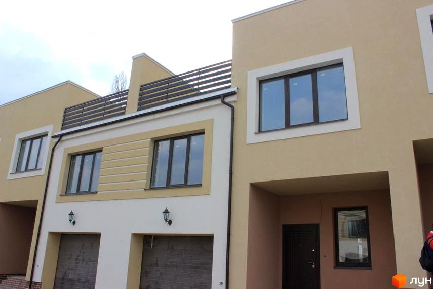 Фасад житлового комплексу на вул. Кибалюка, 17. Будинок має світло-бежевий та білий кольори, великі вікна та гаражні ворота.