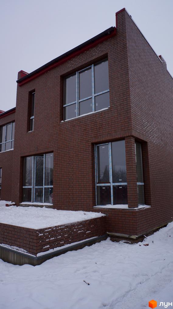 Будинок з коричневої цегли з великими вікнами під час будівництва. Навколо будинку засніжена територія та сніг на даху.