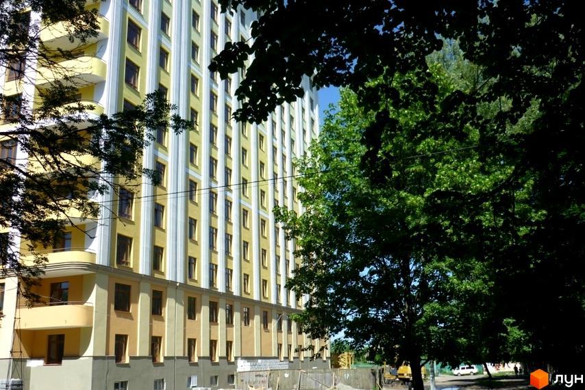 Зображення фасаду багатоповерхового будинку в Житловому комплексі Схід Сонця. Вигляд з вулиці, частково закритий деревами.