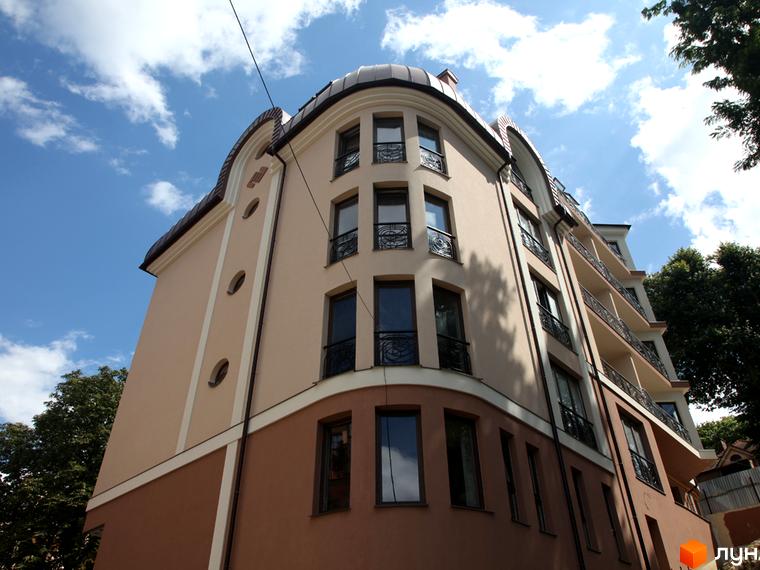 Зображення фасаду будинку на вулиці Братів Тимошенків, 2б. Багатоповерхова будівля з великими вікнами та балконами, розташована на тлі блакитного неба з хмарами.