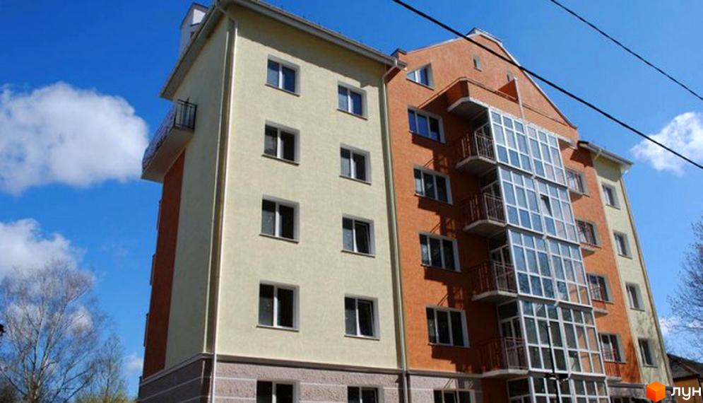Фото фасаду будинку на вулиці Каховська, 26. Житловий комплекс з балконами та великими вікнами на фоні блакитного неба.