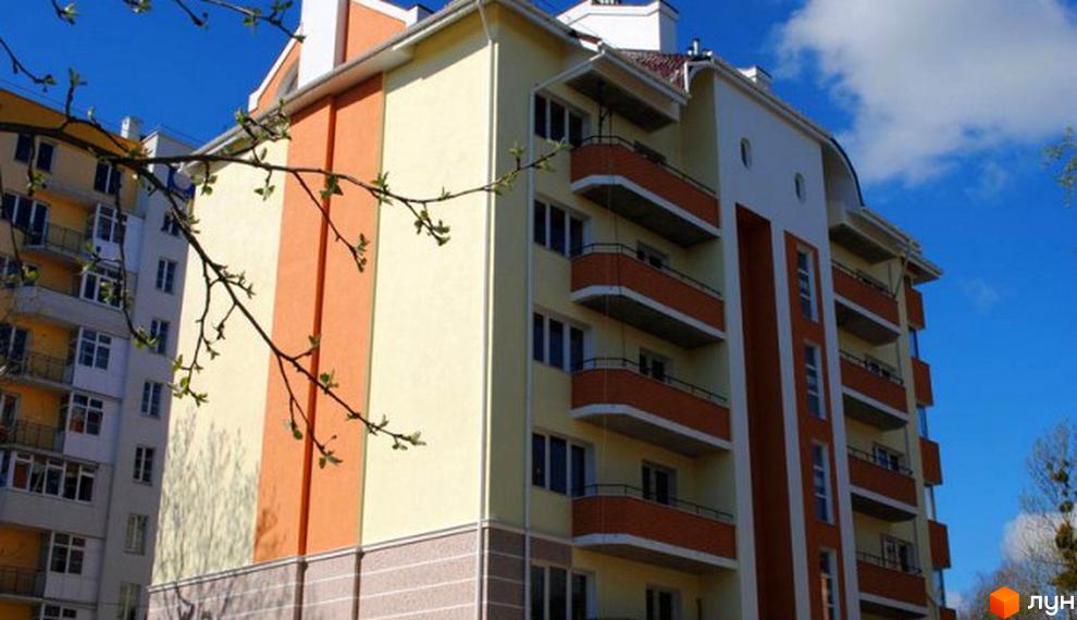 Зовнішній вигляд будинку на вулиці Каховській, 26. Багатоповерхова будівля з балконами та яскравим фасадом. Навколо будинку зелені насадження.