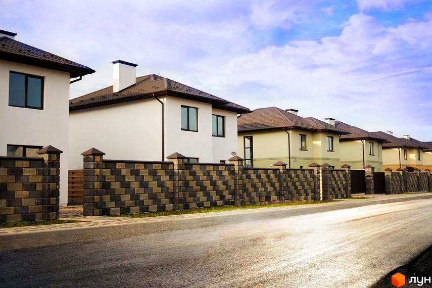 Котеджне містечко Оксамит: ряд однотипних будинків світлого кольору з коричневими дахами та темними вікнами. Перед будинками розташований паркан з двоколірних блоків та дорога.