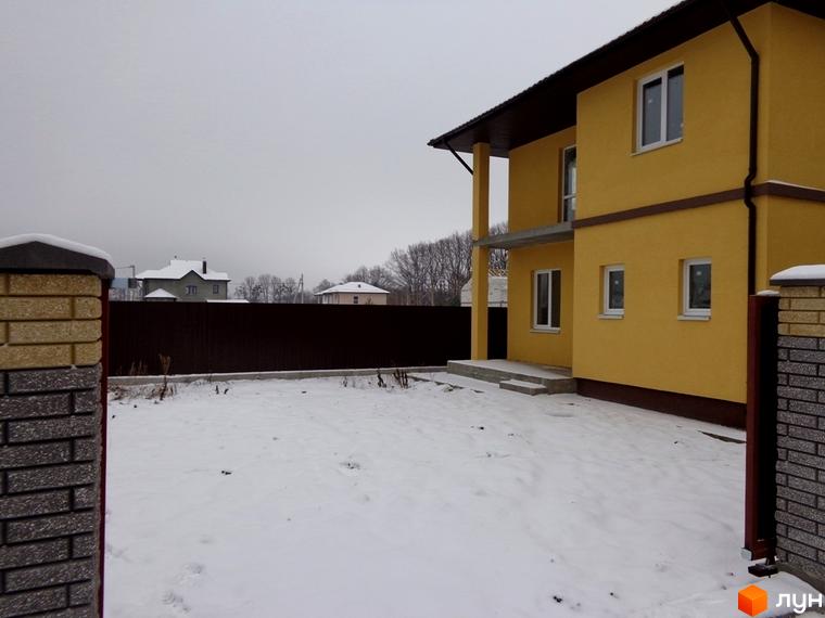 Жовтий двоповерховий будинок з білими вікнами та коричневим дахом у Котеджному містечку Village-Мархалівка. Прибудинкова територія вкрита снігом.