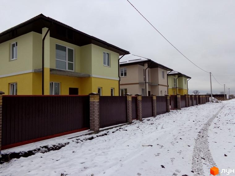 Двоповерхові будинки Котеджного містечка Village-Мархалівка з жовтими фасадами та коричневими дахами. Перед ними засніжена територія з парканом та дорогою.