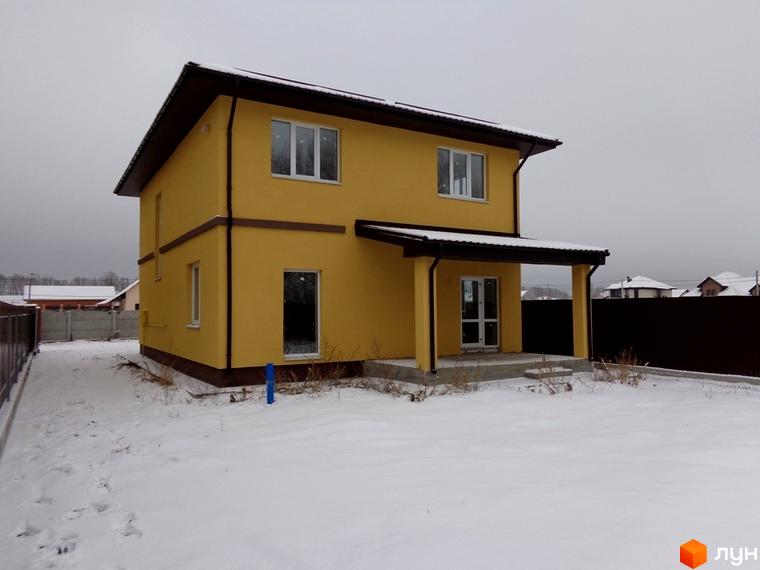 Двоповерховий будинок жовтого кольору з коричневим дахом та ганком у Котеджному містечку Village-Мархалівка. Прибудинкова територія вкрита снігом.