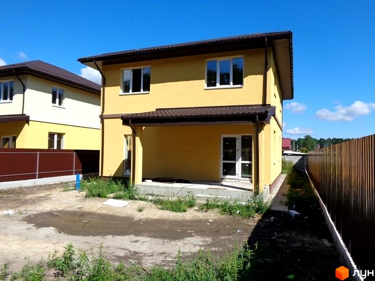 Двоповерховий будинок з жовтими стінами та коричневим дахом в Котеджному містечку Village-Мархалівка. Подвір'я з травою та піском, коричнева огорожа.