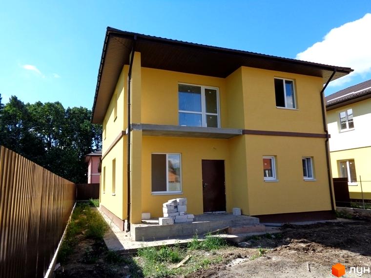 Двоповерховий будинок у Котеджному містечку Village-Мархалівка з жовтим фасадом та коричневим дахом. Навколо будинку зелена трава та дерев'яний паркан.