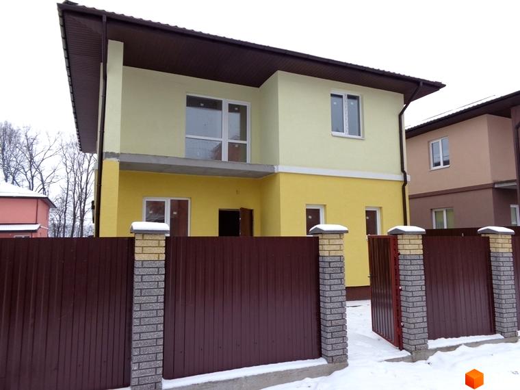 Двоповерховий будинок у Котеджному містечку Village-Мархалівка з коричневим парканом та снігом навколо. Фасад жовтого кольору.