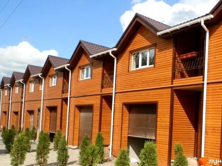 Ряд двоповерхових таунхаусів в П'ятихатках з коричневим сайдингом, білими вікнами та балконами. Перед будинками висаджені зелені декоративні кущі.