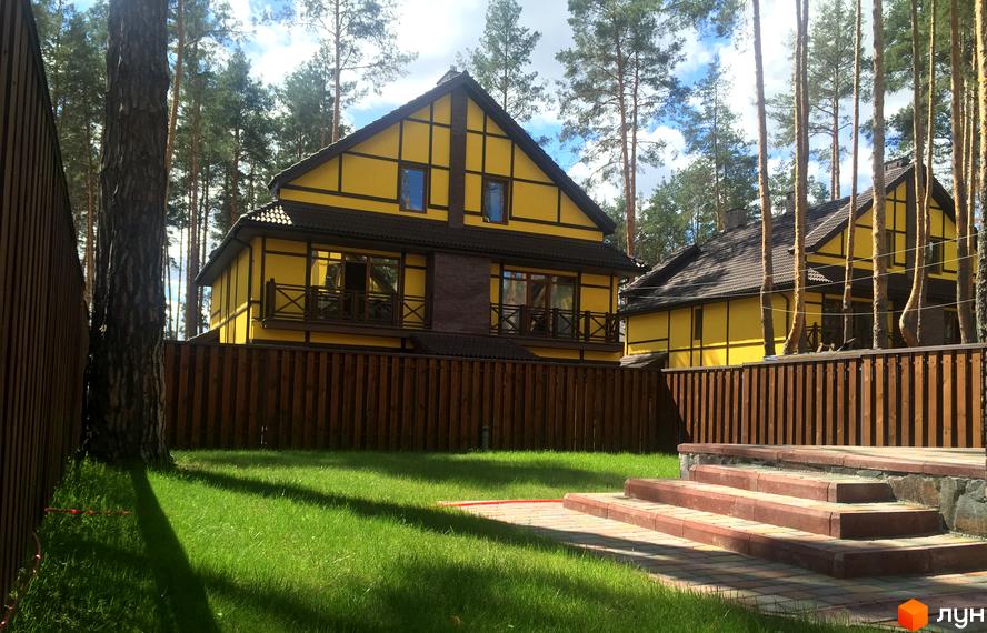 Котеджне містечко Кентербері: жовті будинки з коричневими балкончиками та парканом, зелений газон та сходинки з бруківки. Навколо високі дерева.
