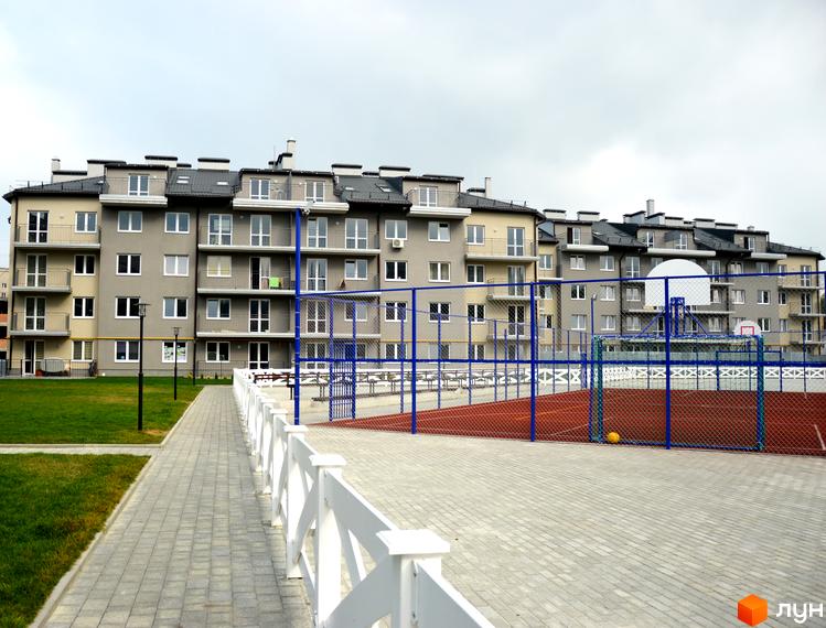 Зовнішній вигляд Житлового комплексу Бельгійське містечко. Багатоповерховий будинок з балконами, поруч дитячий майданчик та тротуарна доріжка.