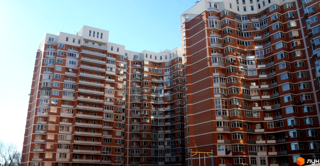 Зовнішній вигляд будинку ЖК Романівський з балконами та великими вікнами. Прибудинкова територія з дитячим майданчиком та зеленими насадженнями.