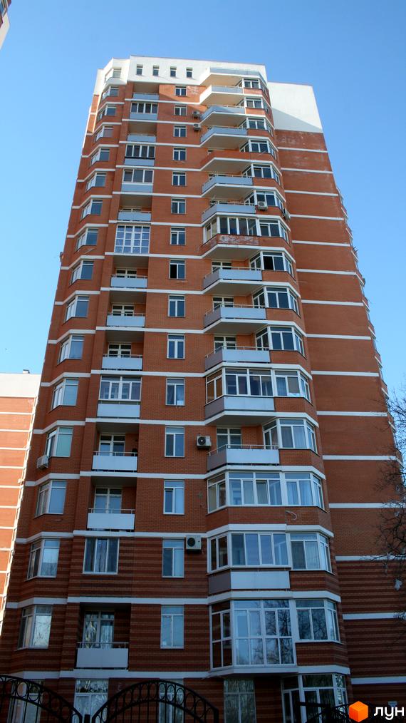 Вигляд будинку житлового комплексу Романівський з балконами та великими вікнами. Прибудинкова територія з зеленими насадженнями.