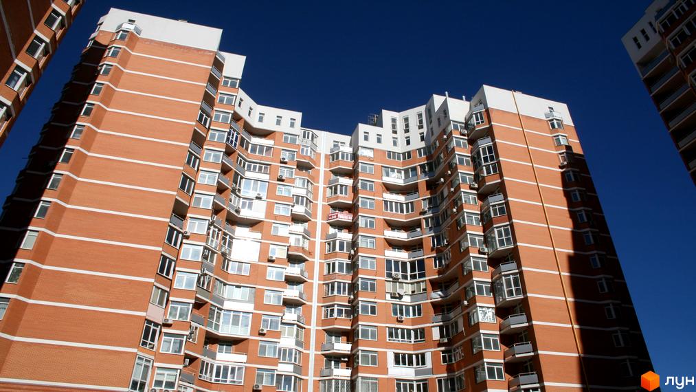 Житловий комплекс Романівський з червоною цегляною фасадою та балконами. Прибудинкова територія з зеленими насадженнями.