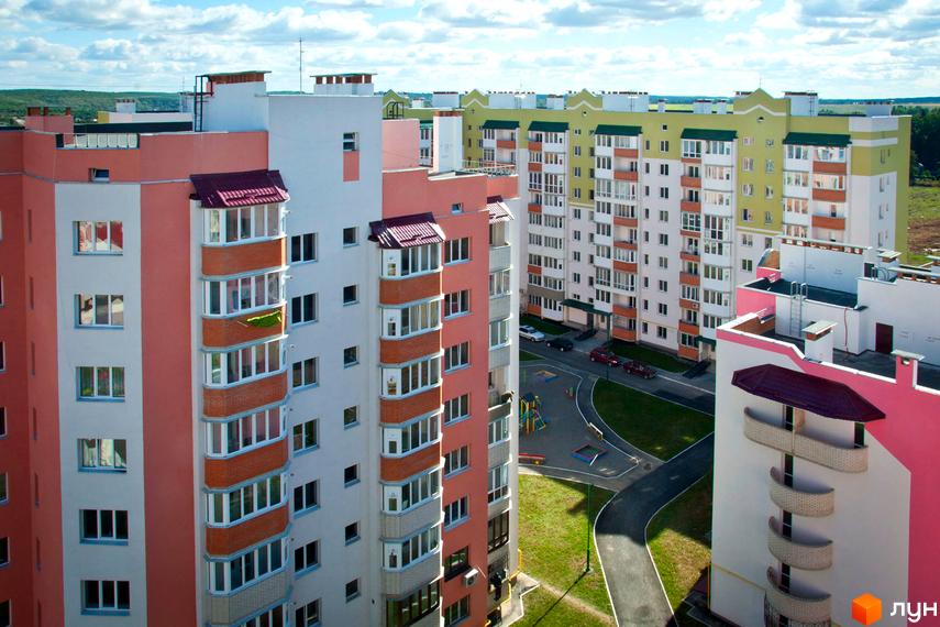 Житловий комплекс Мікрорайон „Поділля“ – багатоповерхові будинки з рожевими та білими фасадами, зеленою покрівлею, поруч дитячий майданчик.