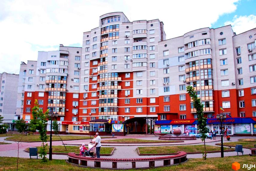 Зовнішній вигляд багатоповерхового житлового комплексу Мікрорайон „Поділля“ з червоно-сірим фасадом та прибудинковою територією з ландшафтним дизайном.