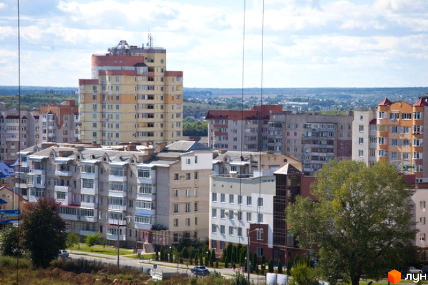 Вид на житловий комплекс Мікрорайон „Поділля“ з багатоповерховими будинками різної висоти та кольорової гами. На передньому плані видно зелені насадження та дорогу.