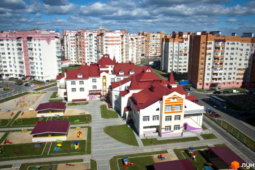 Вид на житловий комплекс Мікрорайон „Поділля“ з багатоповерховими будинками та дитячим садком з червоним дахом. На території комплексу розташовані дитячі майданчики та зелені зони.
