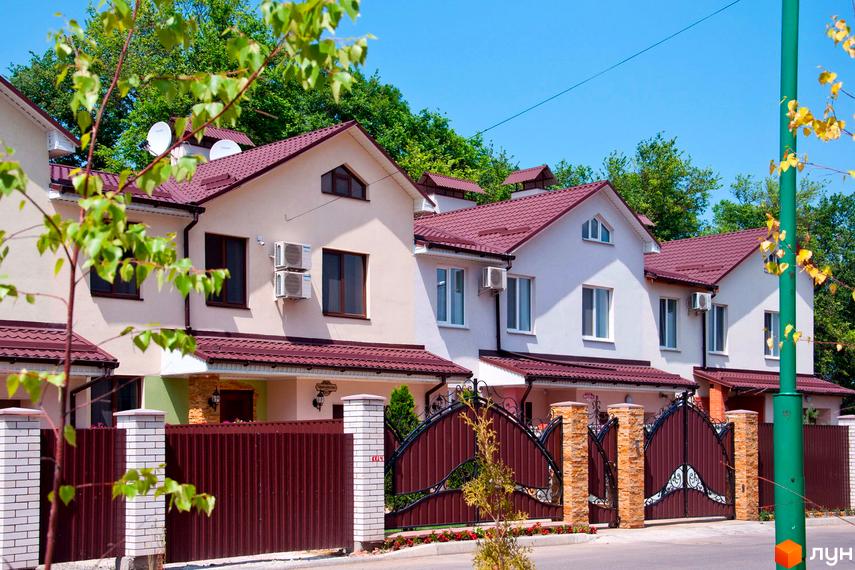 Зовнішній вигляд сучасних будинків житлового комплексу Мікрорайон „Академічний“ з червоними дахами та парканами. На території комплексу розташовані зелені насадження та дерева.