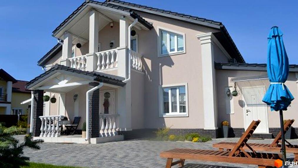 Зображення двоповерхового будинку в Котеджному містечку Family House. На передньому плані тераса з лежаками та парасолькою.