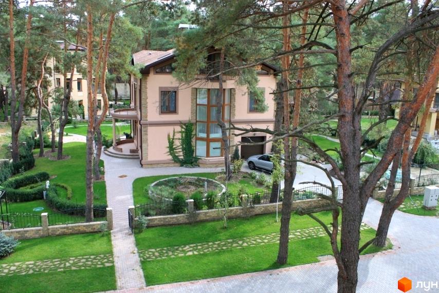 Двоповерховий будинок з великими вікнами та гаражем. На території Котеджне містечко Шишкино доглянутий газон, доріжки та дерева.