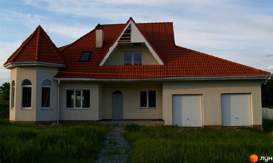 Зображення фасаду будинку з червоною черепичною покрівлею та гаражами. Перед будинком газон та доріжка.