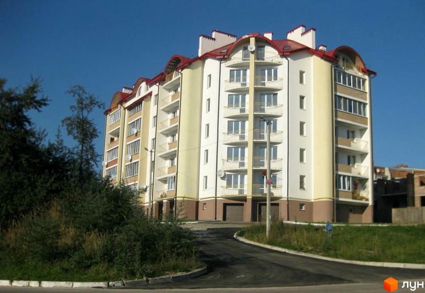 Фото фасаду багатоквартирного будинку по вулиці Джона Леннона, 37. Навколо будинку зелена прибудинкова територія та асфальтована дорога.