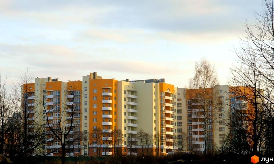 Багатоповерхові житлові будинки оранжевого та світло-жовтого кольорів з білими балконами на вул. Червоної Калини, 72, 72а. Навколо видно голі дерева.