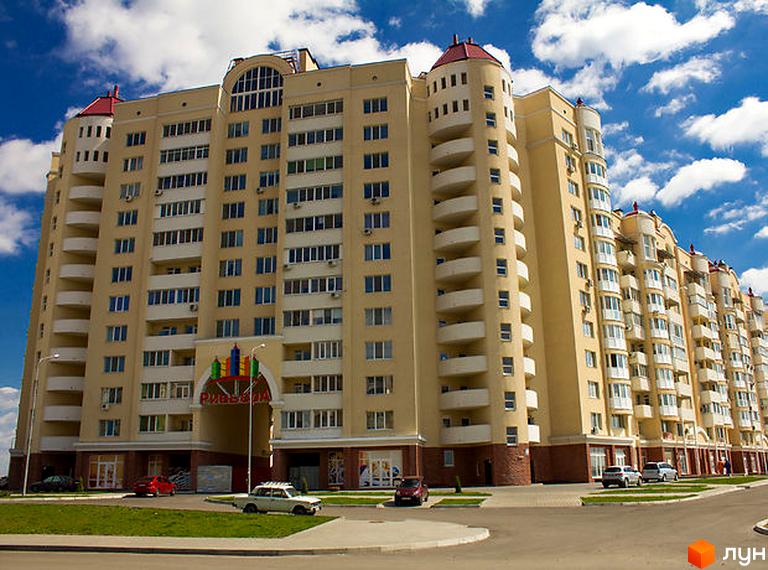 Житловий комплекс Рів'єра – багатоповерховий будинок жовтого кольору з численними балконами та арочним входом. Навколо комплексу розташовані зелені насадження та дороги.