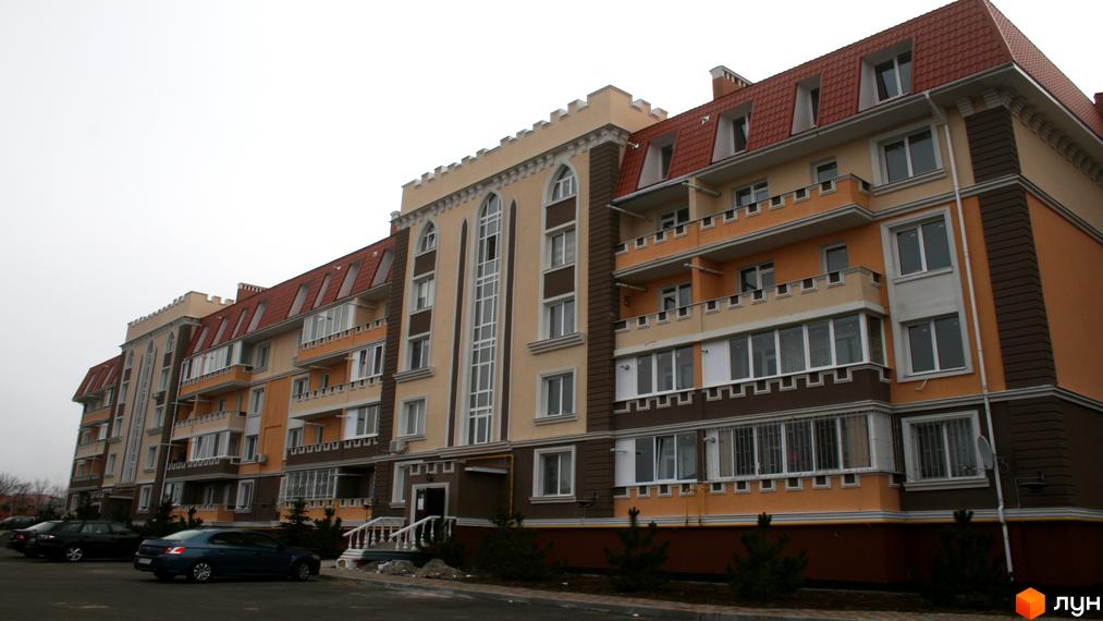 Житловий комплекс Академгородок-Совиньон: багатоповерхова будівля зі світло-бежевим фасадом, помаранчевими елементами та червоним дахом. Перед будинком облаштована парковка.