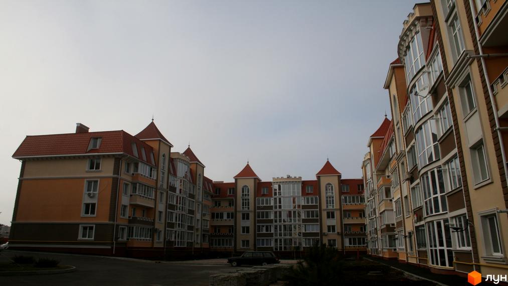 Зовнішній вигляд житлового комплексу Академгородок-Совиньон з багатоповерховими будинками та червоними дахами. На прибудинковій території видно дорогу та зелені насадження.