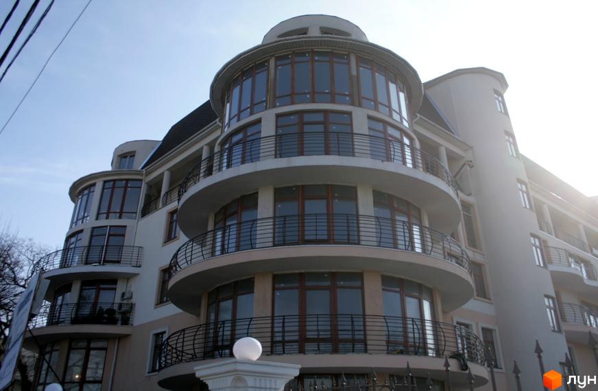 Багатоповерховий будинок ЖК Лазурний берег з балконами та круглими вікнами. Видно ковані огорожі та білий декор.