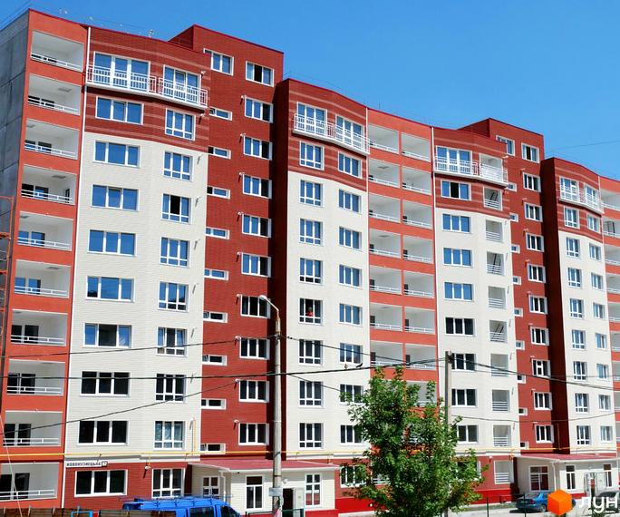 Новобудова за адресою вул. Володимира Українця (Новокузнецька), 72-75, має багатоповерховий фасад у червоно-білих кольорах з численними балконами. Поруч видно зелені насадження.