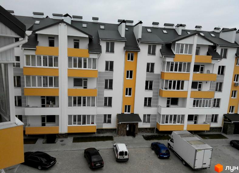 Житловий комплекс Сонячний майдан з білим фасадом, жовтими балконами та сірою покрівлею. На прибудинковій території видно припарковані автомобілі.
