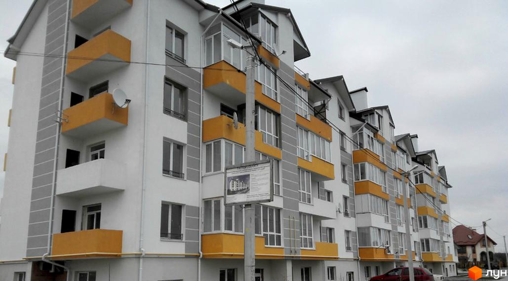 Новобудова Сонячний майдан з біло-сірим фасадом та жовтими балконами. На фото видно вулицю та припаркований автомобіль.