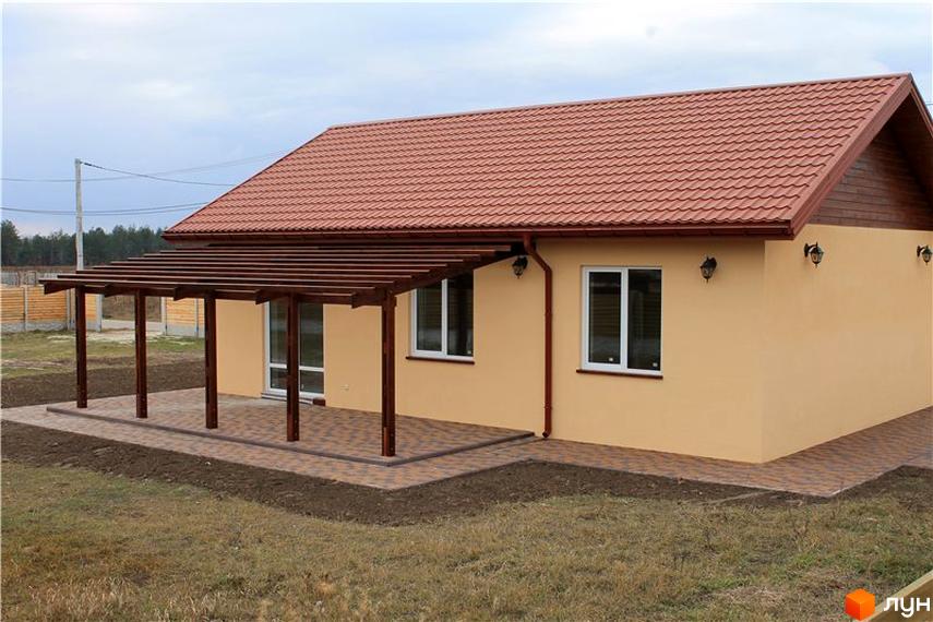 Котеджне містечко Рябинки: одноповерховий будинок з червоним дахом, світло-жовтими стінами та дерев'яною верандою. Навколо будинку викладена бруківка та доглянута ділянка.