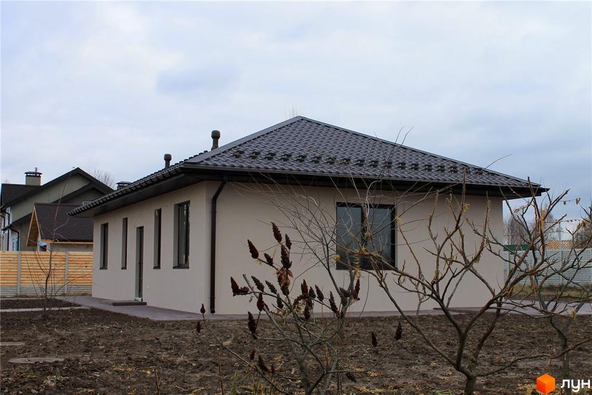 Одноповерховий будинок з коричневим дахом та світлими стінами. Навколо будинку доглянута прибудинкова територія з деревами та огорожею.