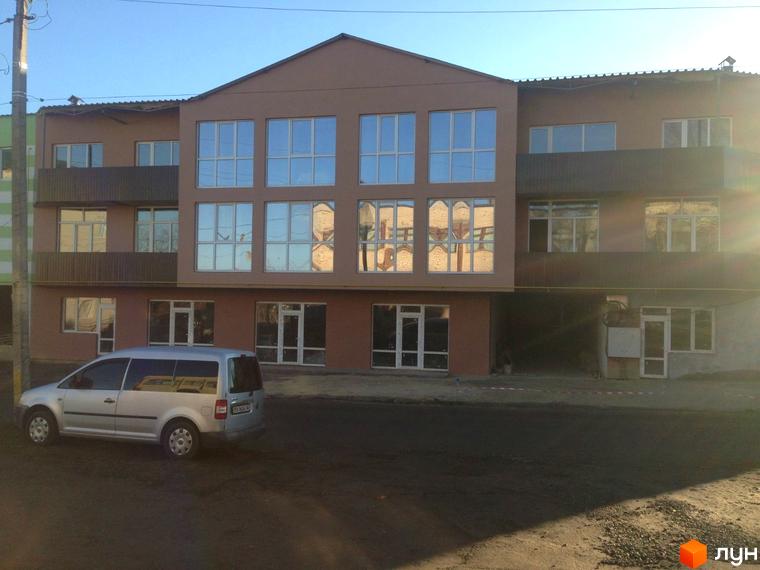 Зовнішній вигляд будинку в Житловому комплексі Фамільний двір. Багатоповерхова будівля з великими вікнами, поруч припаркований автомобіль.