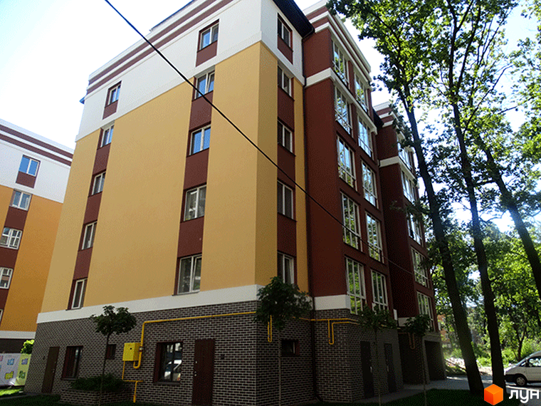 Житловий комплекс Затишний: багатоповерховий будинок з жовтим, темно-червоним фасадом та сірою цегляною основою. Прибудинкова територія озеленена деревами.