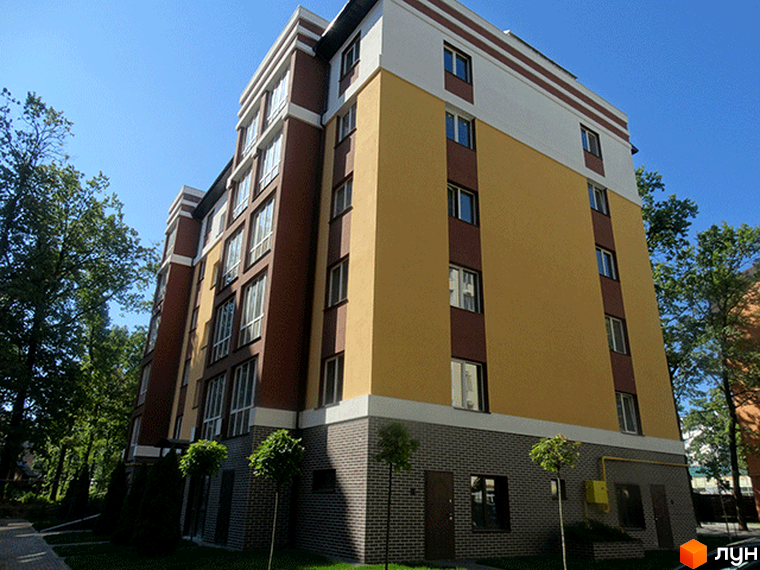 Житловий комплекс Затишний: багатоповерховий будинок з жовто-коричневим фасадом та сірою цегляною основою, оточений зеленими деревами.