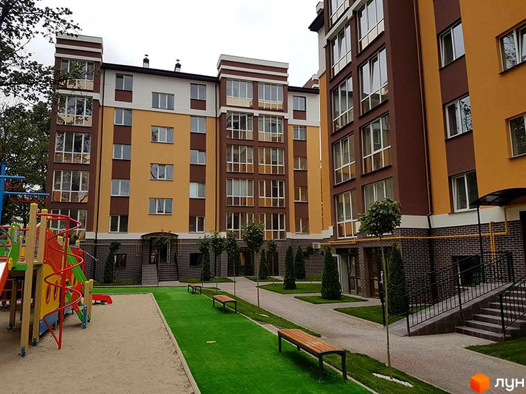 Зовнішній вигляд багатоповерхового будинку в Житловому комплексі Затишний. На території є дитячий майданчик, лавки та зелені насадження.
