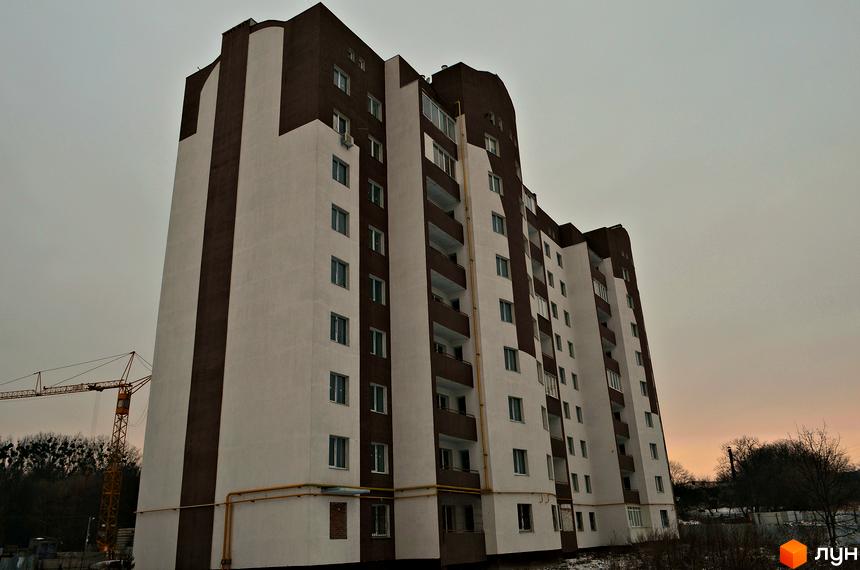 Зовнішній вигляд новобудови на вул. Академіка Сахарова, 14б. Будинок має біло-коричневе оздоблення фасаду. На задньому плані видно будівельний кран.