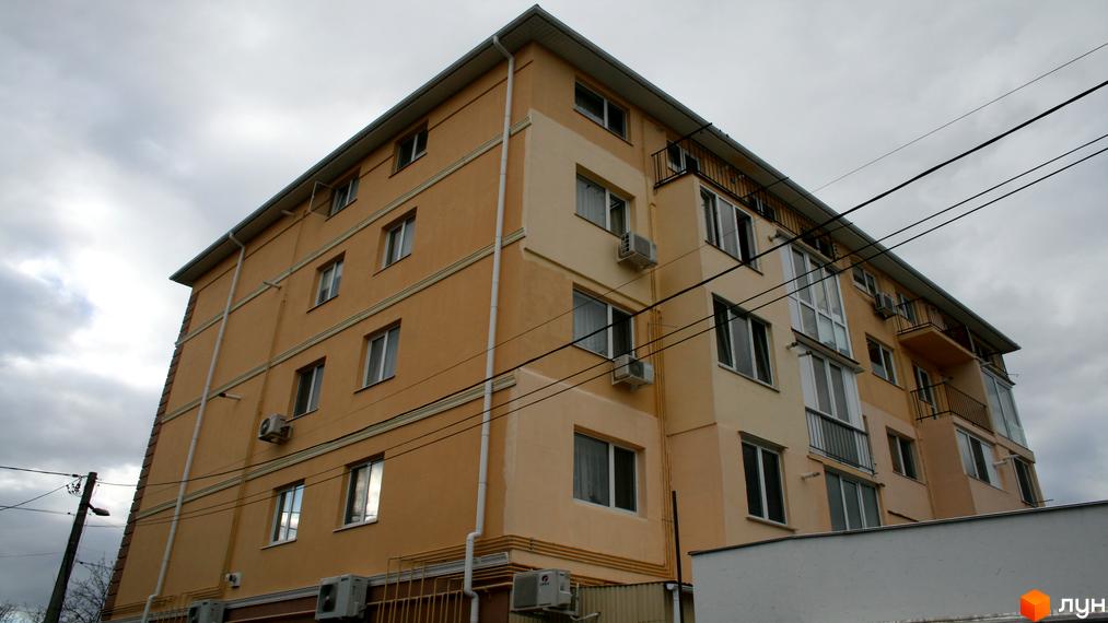 Житловий комплекс Затишний дім: багатоповерхова будівля з оранжевим фасадом та вікнами. Навколо видно електричні дроти та вуличне освітлення.